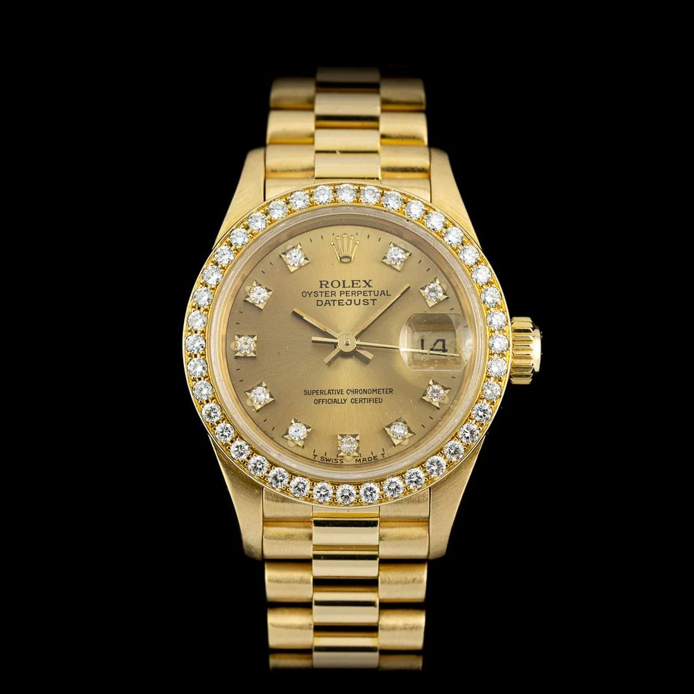 A gold wristwatch with a diamond bezel, spotlit on a black background.